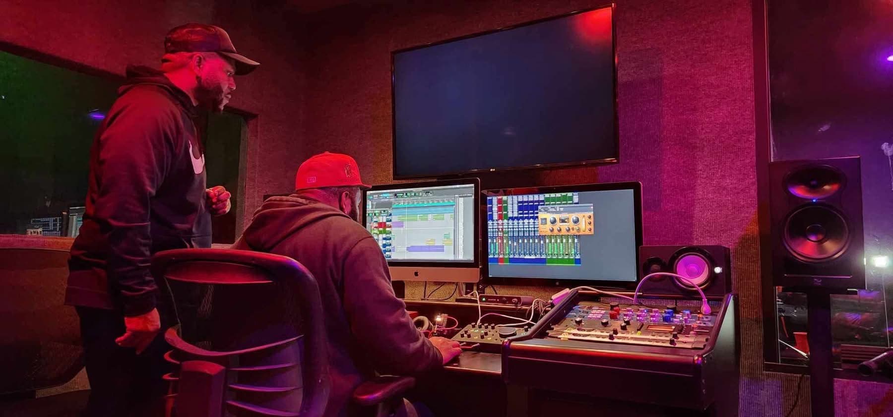 Engineer and client at the JaxCity Studios console under magenta session lighting